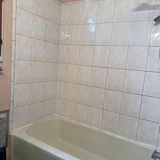 A bathroom with a bathtub , shower , and tiled walls.