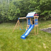 A wooden playground set with a blue slide and swings in a backyard.