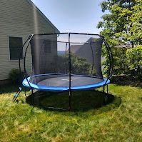 A blue trampoline is sitting in the grass in front of a house.
