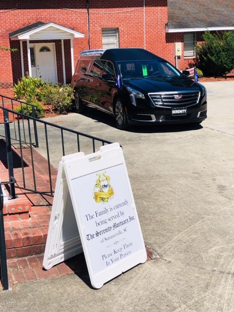A funeral hearse parked outside a brick building next to a sign that reads, 