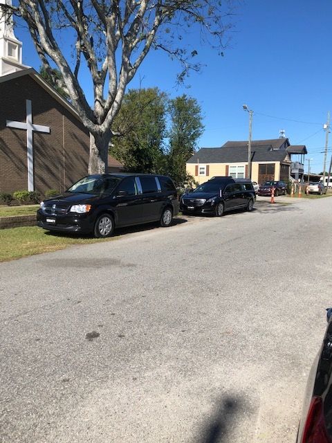Two black hearses parked on the side of a street next to a brick church with a white cross.