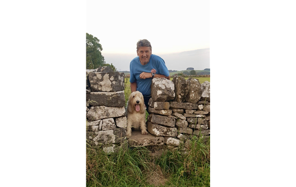 A man and a dog are sitting on a stone wall.