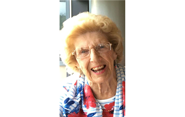 An elderly woman wearing glasses and a floral shirt is smiling for the camera.