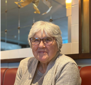 An elderly woman wearing glasses is sitting at a table in a restaurant
