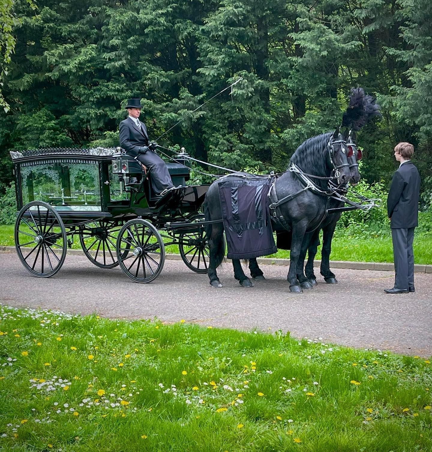 A man in a top hat stands next to a horse drawn carriage