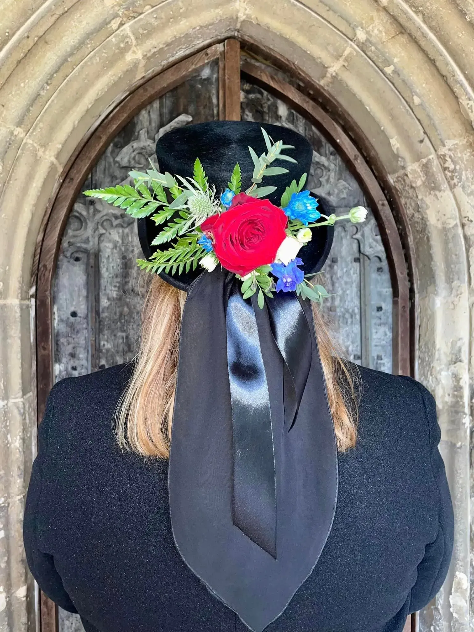 A woman wearing a top hat with flowers on it is standing in front of a door.