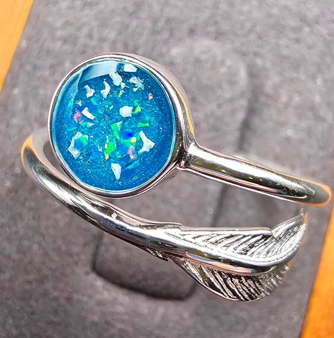 A silver ring with a blue stone and a feather on it