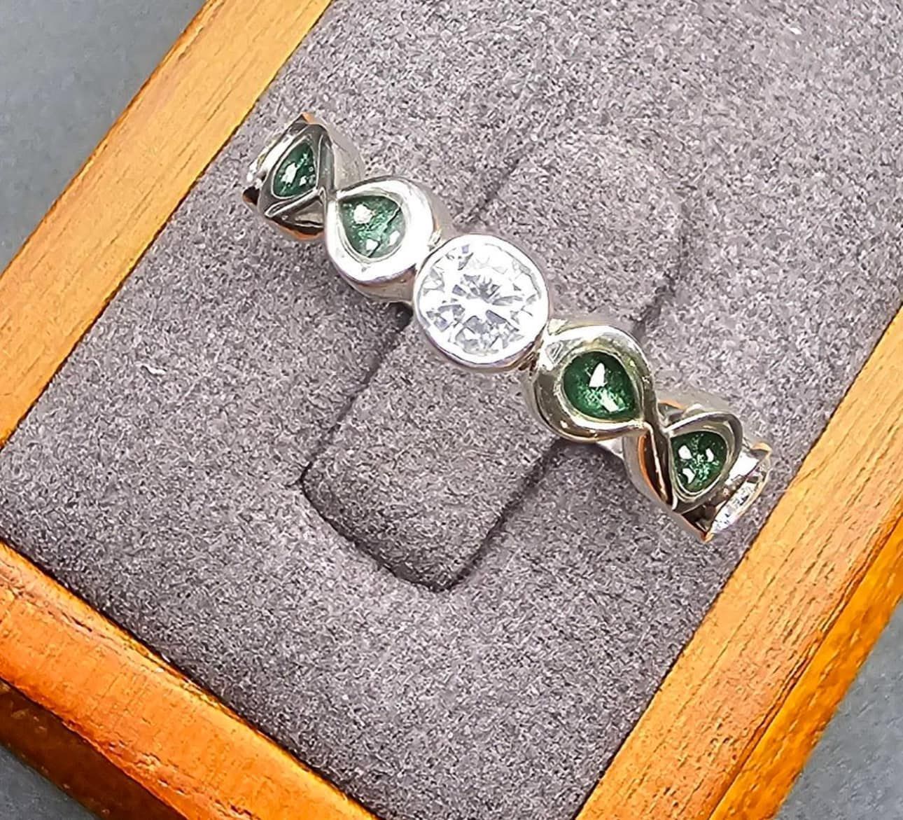 A ring with emeralds and diamonds is sitting in a wooden box.