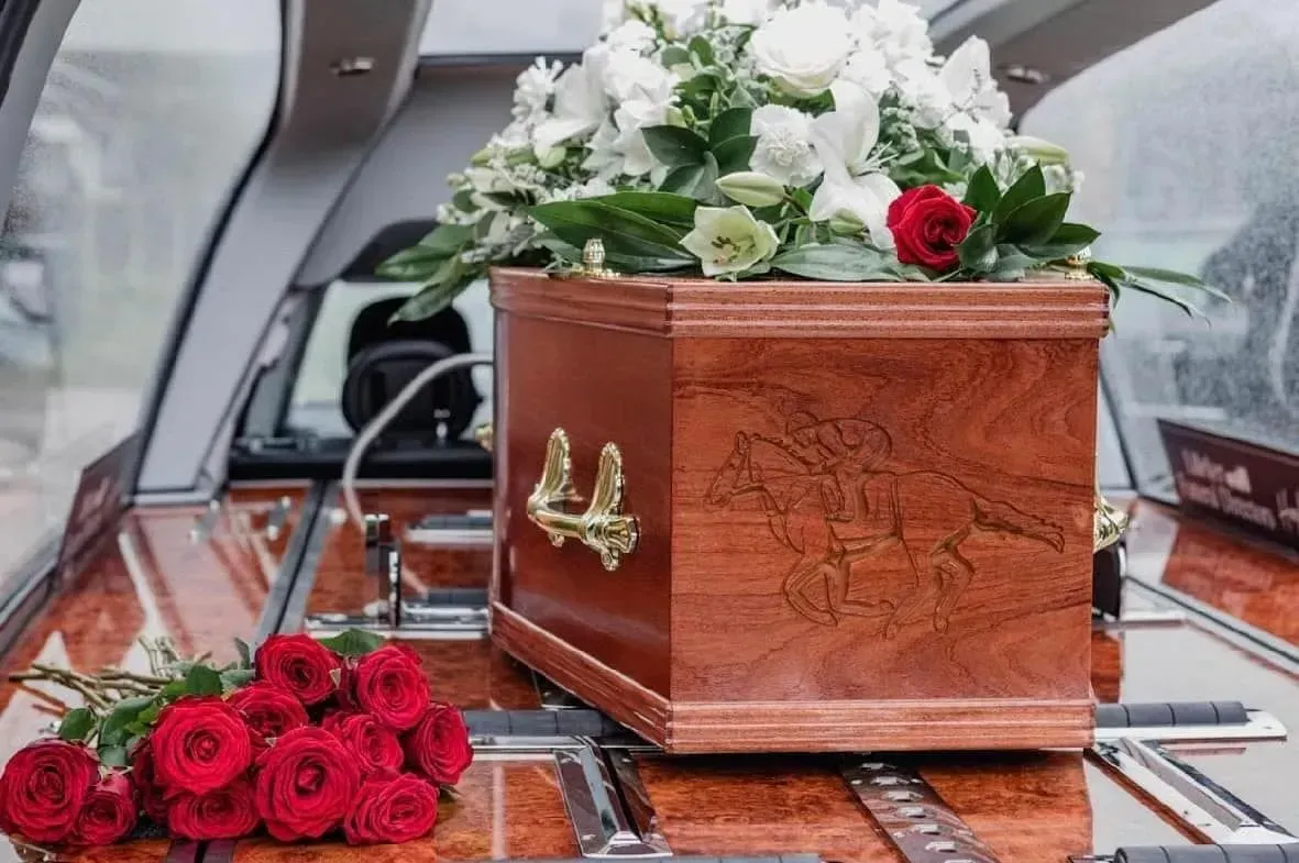 A wooden coffin filled with flowers is in a funeral car.