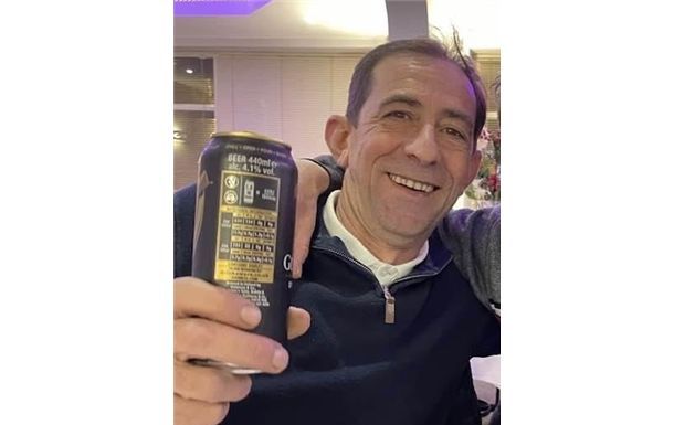 A man is sitting at a table holding a can of beer.