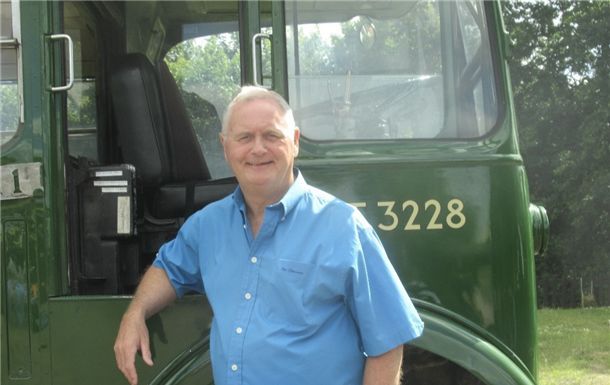 A man in a blue shirt stands in front of a green truck with the number 3228 on it