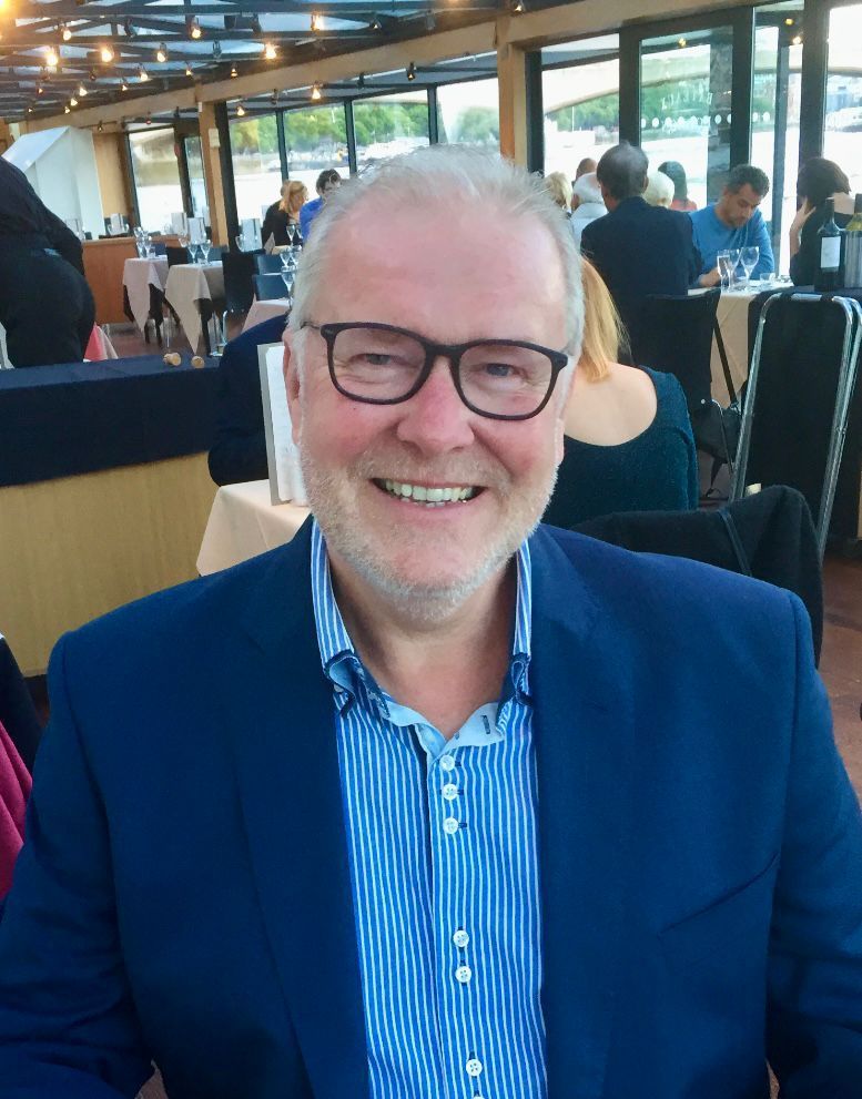 A man wearing glasses and a blue jacket smiles for the camera