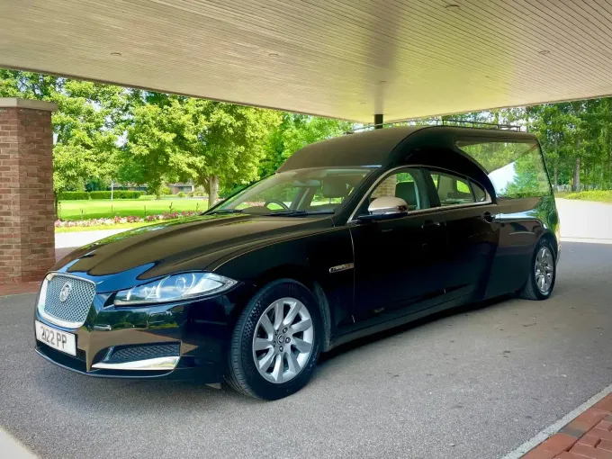 Black Jaguar hearse parked under a canopy.