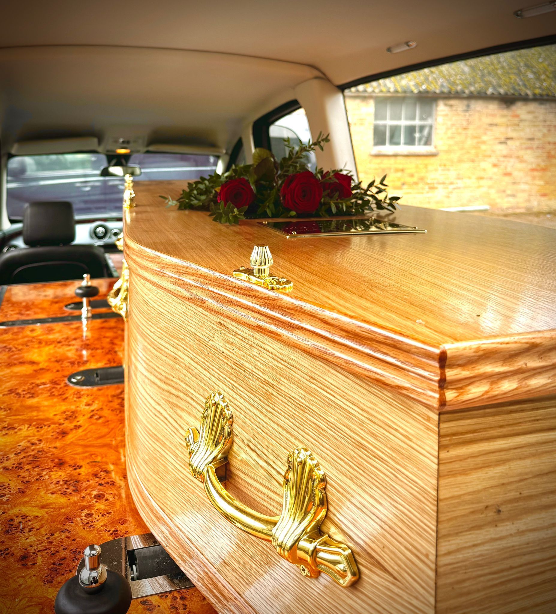 A wooden coffin with gold handles sits in the back of a car