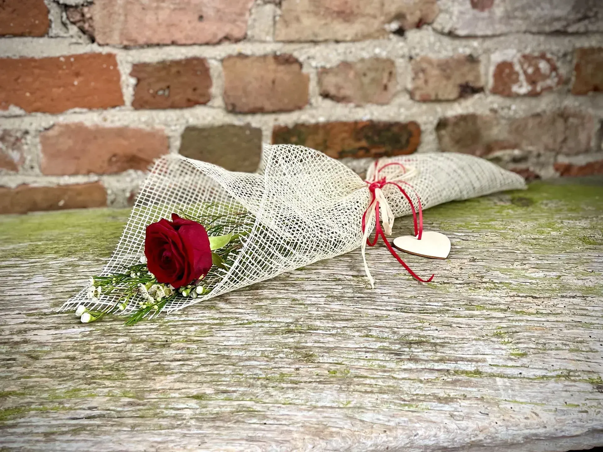 A red rose is wrapped in white lace and tied with a red string