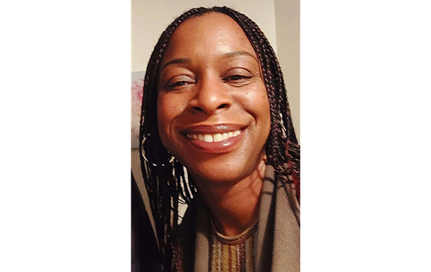 Man wearing sunglasses, hat, and Star Wars Adidas jacket, sitting inside at a table near a window.
