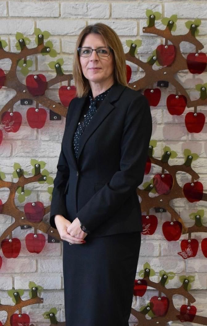 Woman in black suit stands in front of a wall with apple tree decorations.