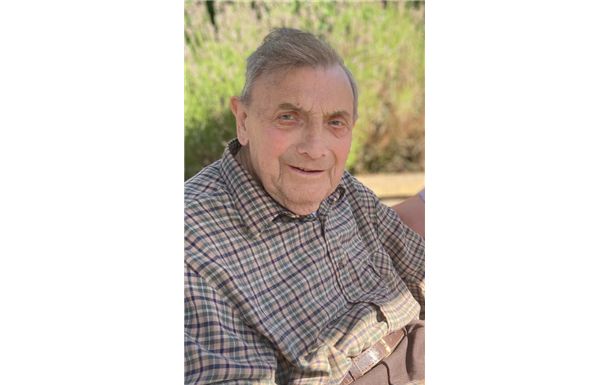 A man in a plaid shirt is sitting on a bench and smiling.