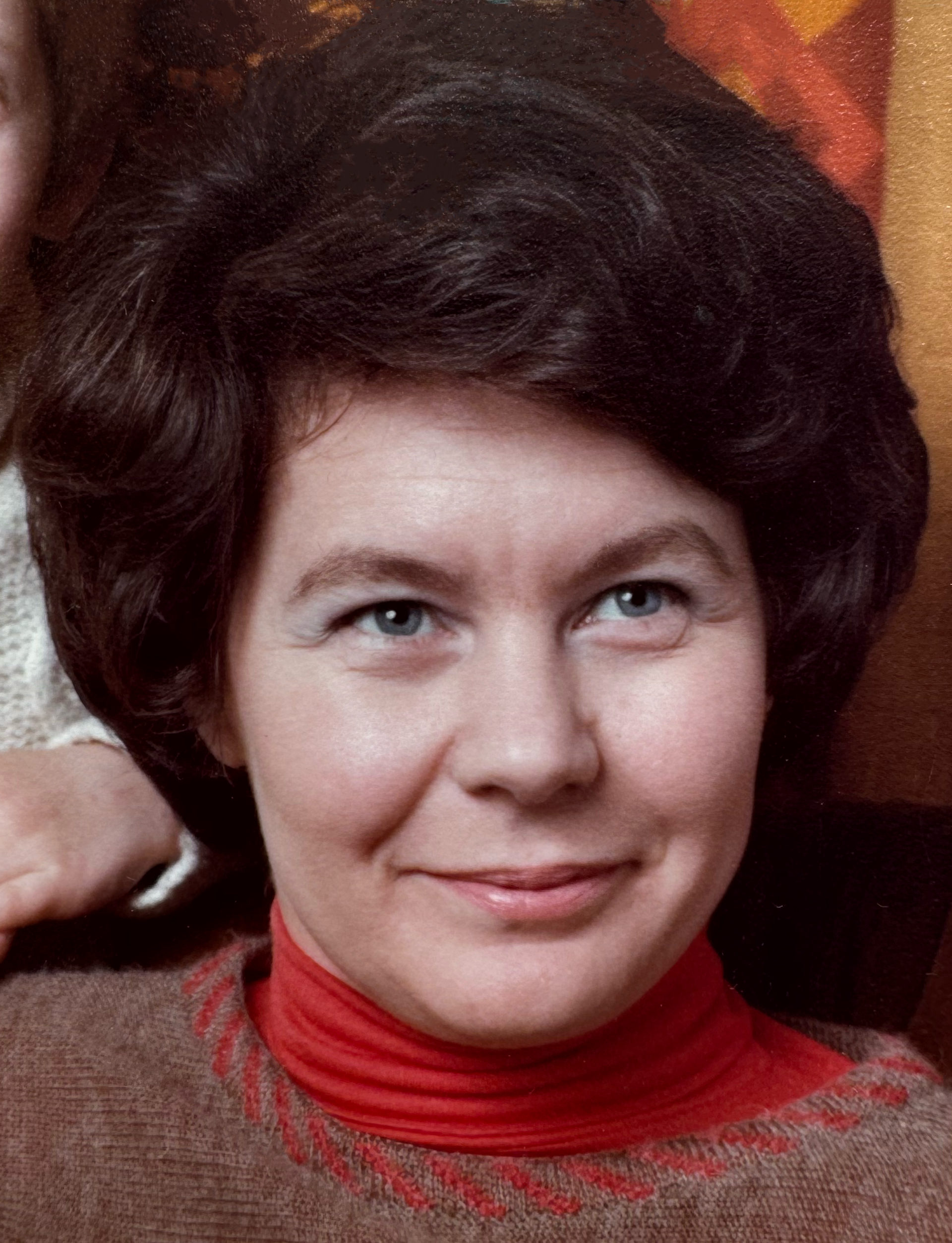 A woman wearing a red turtleneck smiles for the camera