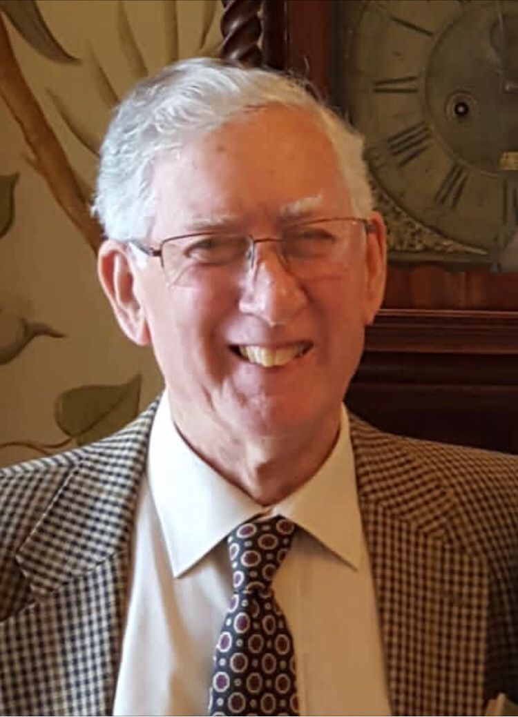 A man in a suit and tie is smiling in front of a clock