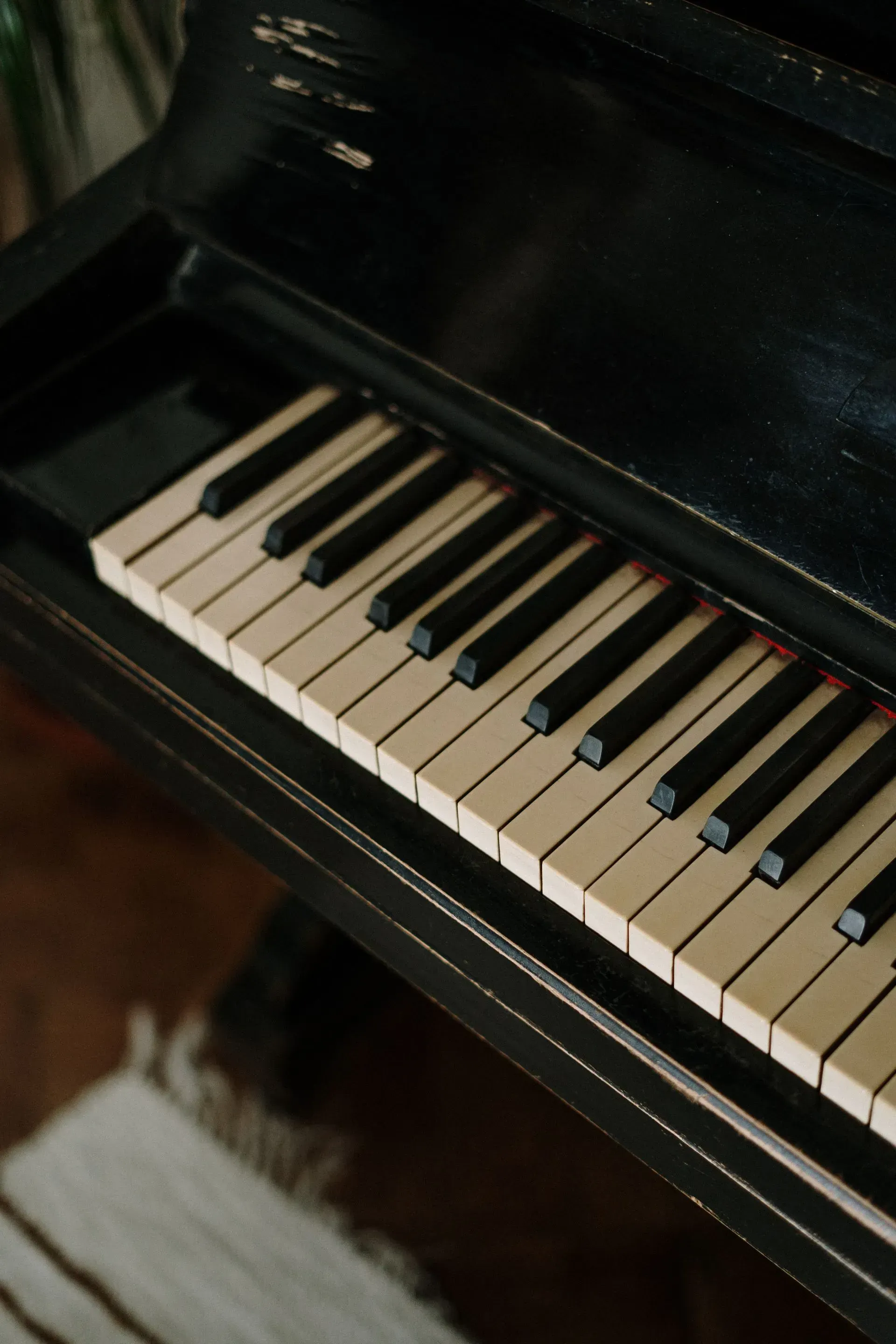 A black piano with white keys is sitting on a wooden floor.