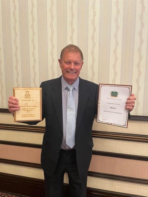 A man in a suit and tie is holding two awards