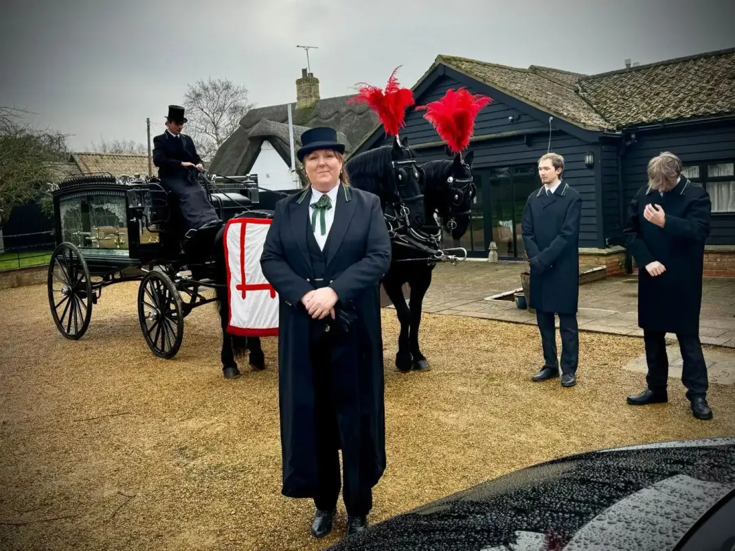 A horse-drawn hearse with attendants, preparing for a funeral outside a building.
