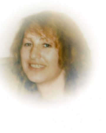 Head-and-shoulders portrait of a person with light brown hair, smiling gently against a soft, faded white background.