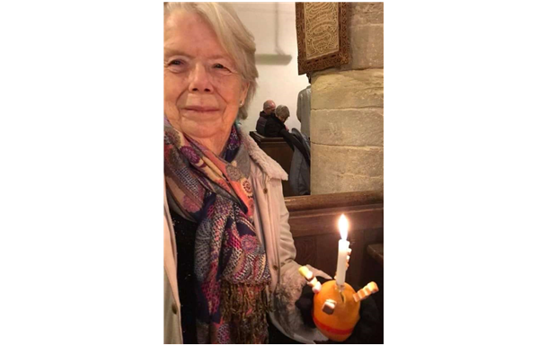 Woman holding lit candle with orange decoration inside church.
