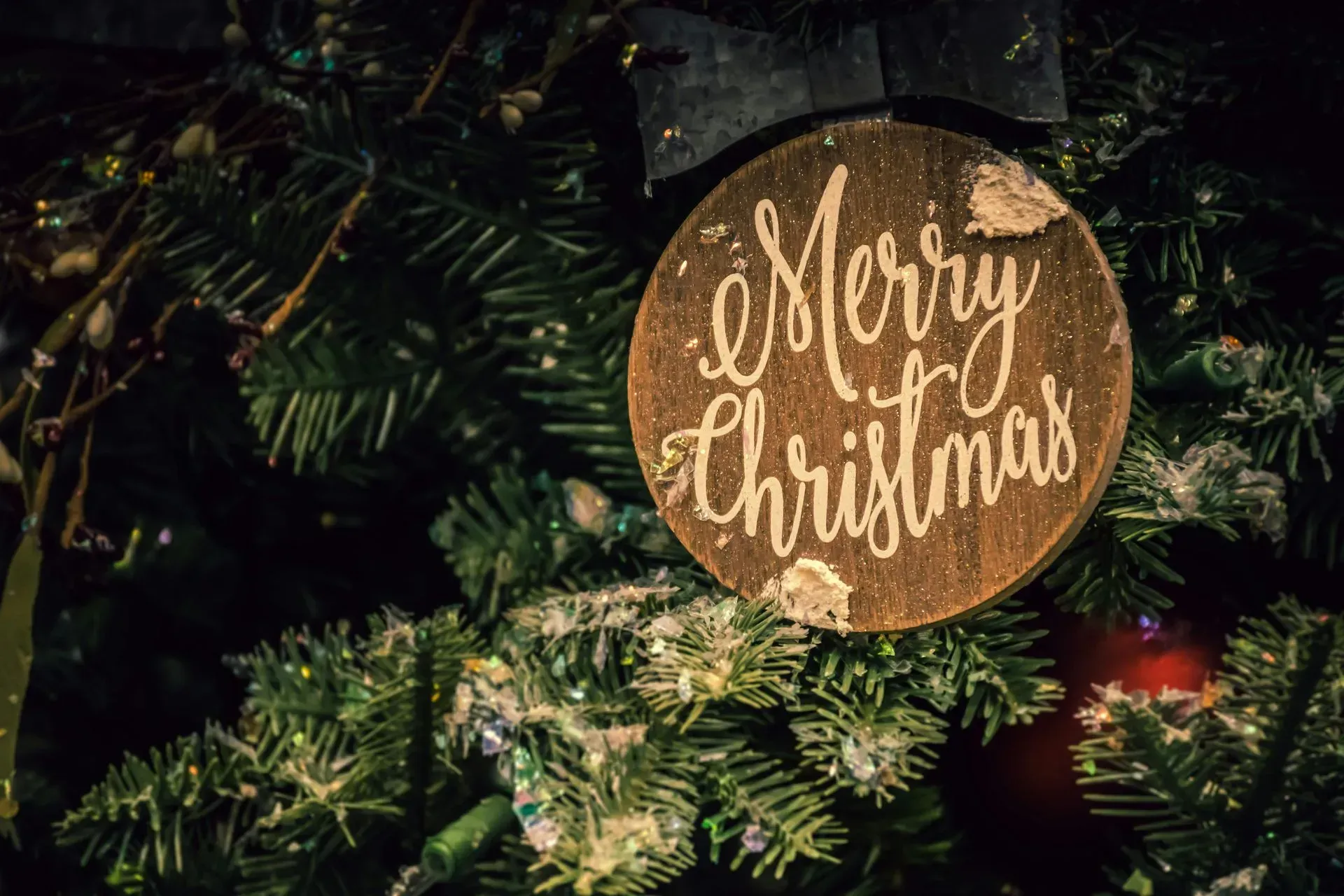 A merry christmas ornament hangs from a christmas tree