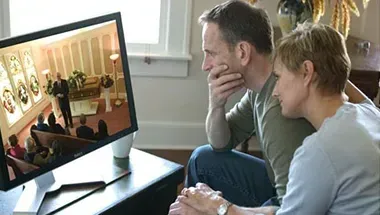 A man and a woman are sitting on a couch looking at a computer screen.