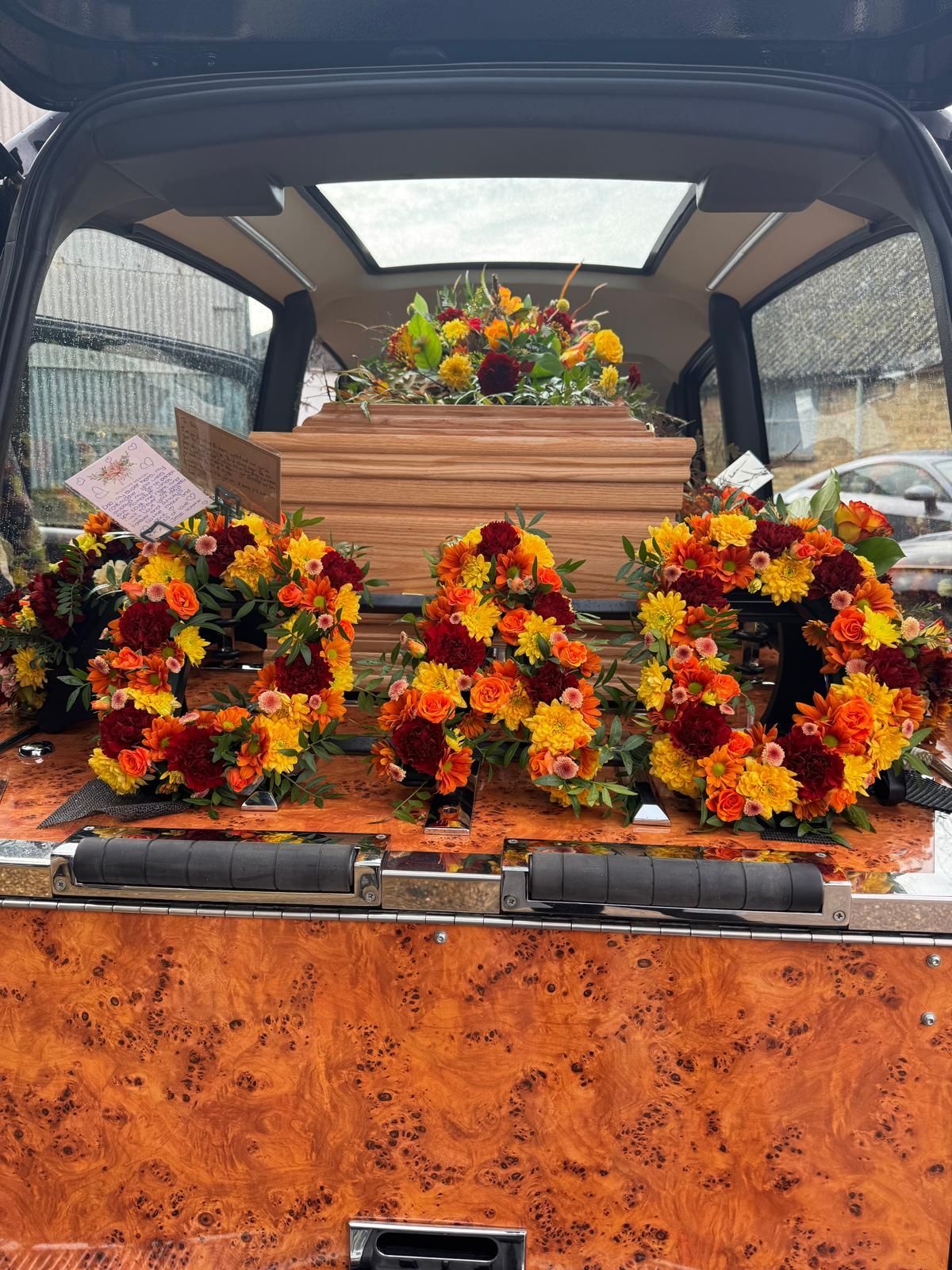 Hearse interior with a wooden casket and floral arrangements spelling