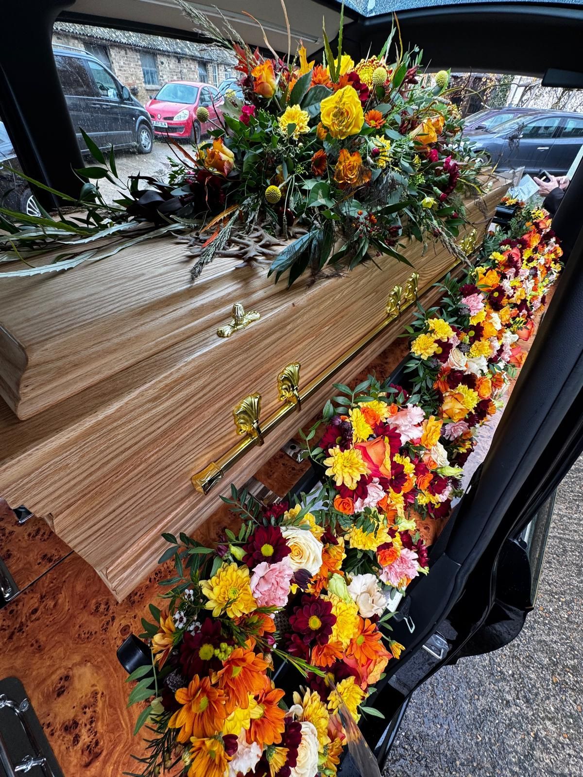Coffin in hearse, adorned with colorful floral arrangements of yellow, orange, and red.