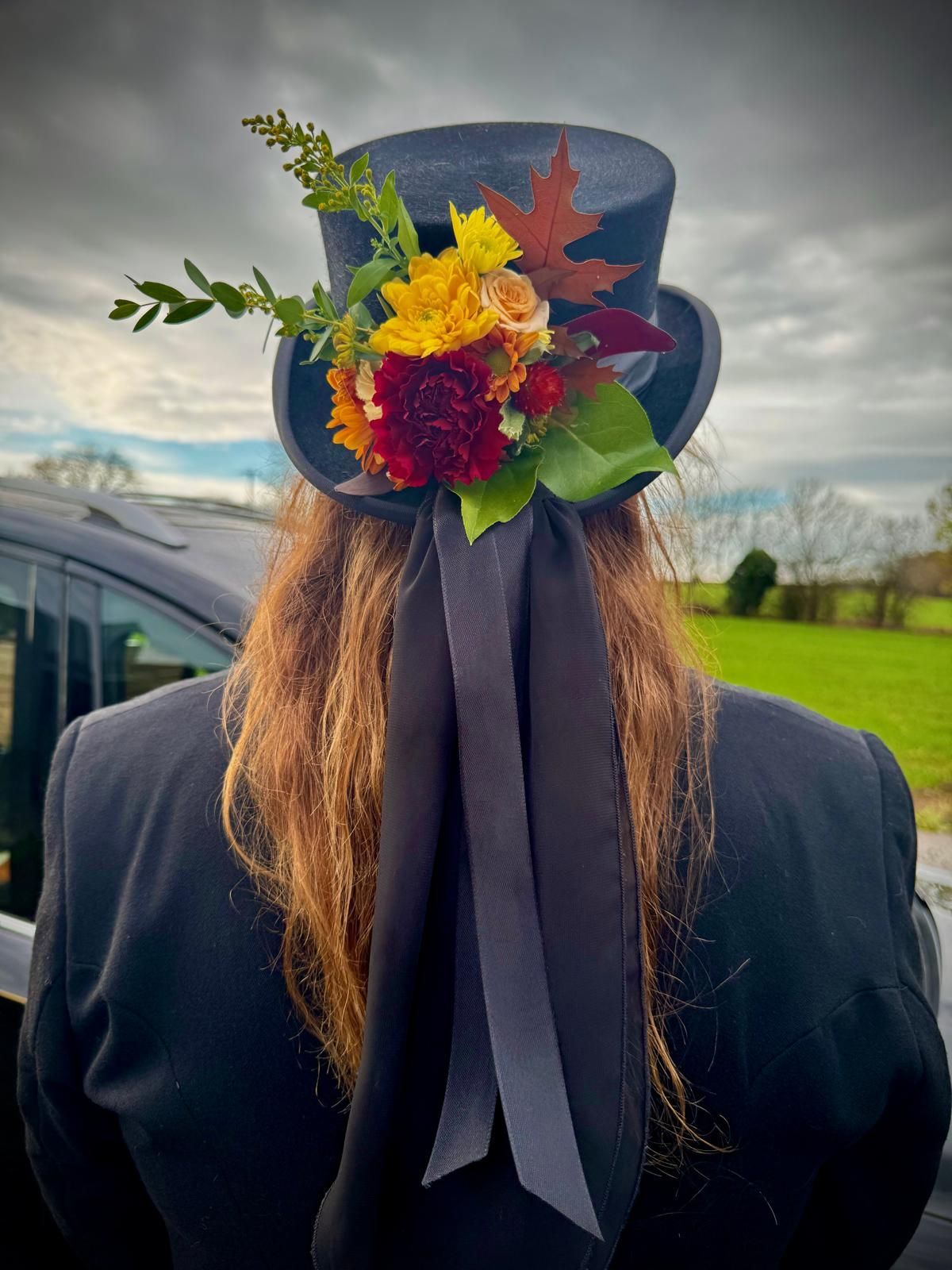 Person wearing a black top hat adorned with autumn flowers and a black ribbon.