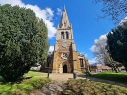 A large church with a steeple is surrounded by trees on a sunny day.