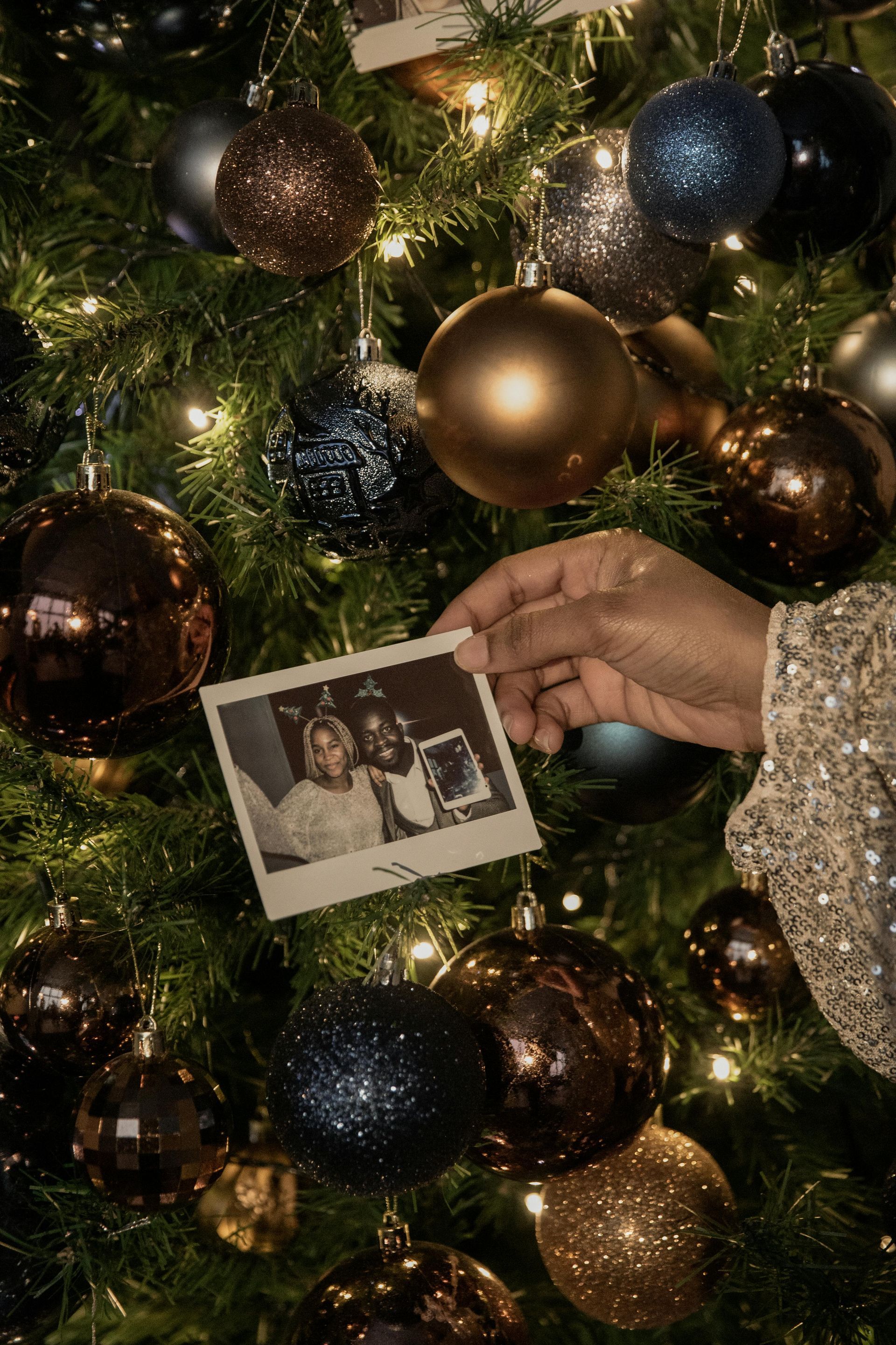 Hand holding a photo next to a decorated Christmas tree with ornaments.