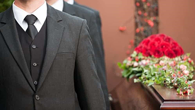 A group of men in suits and ties are carrying a coffin at a funeral.