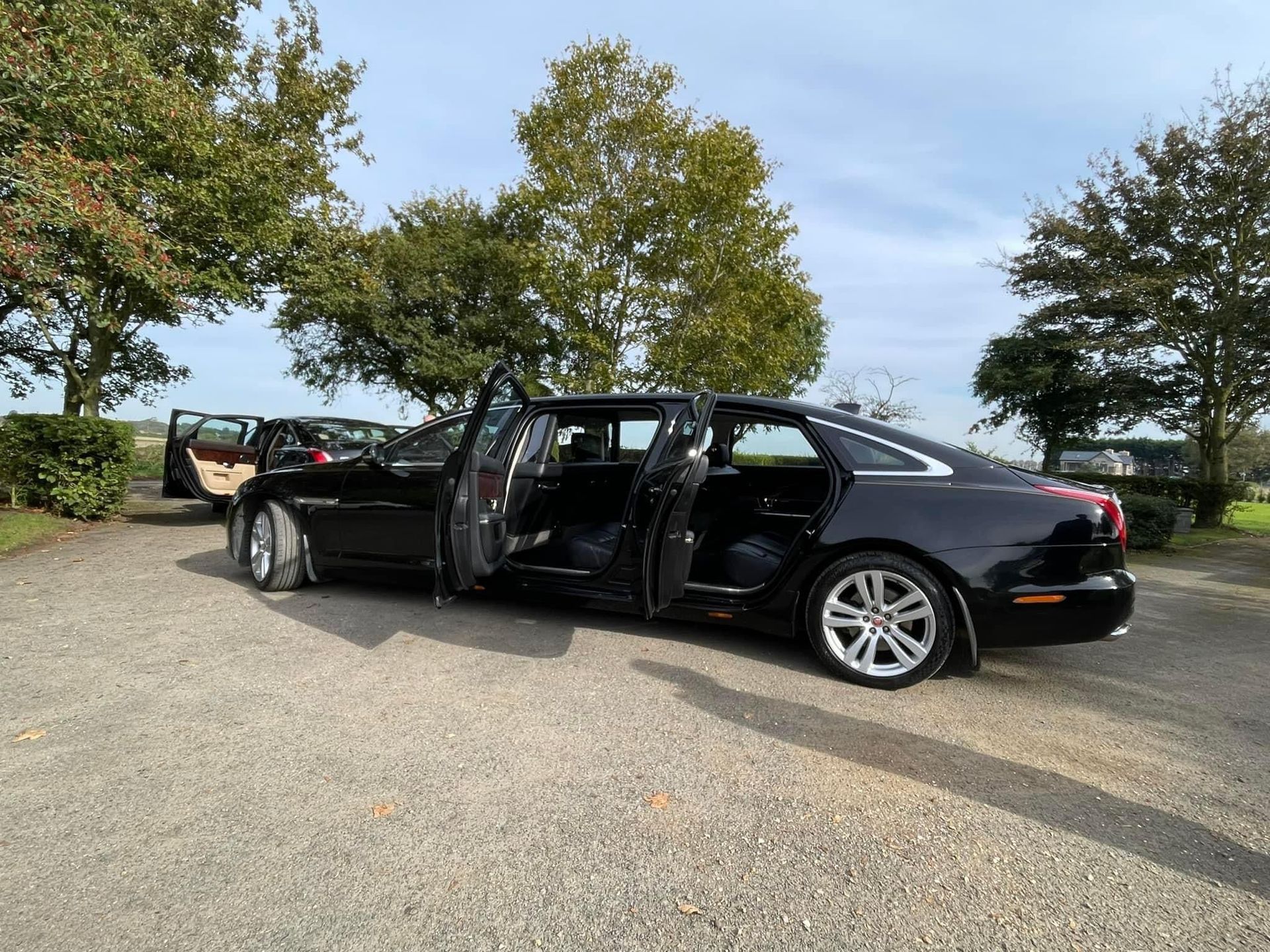 A black car with its doors open is parked in a gravel driveway.