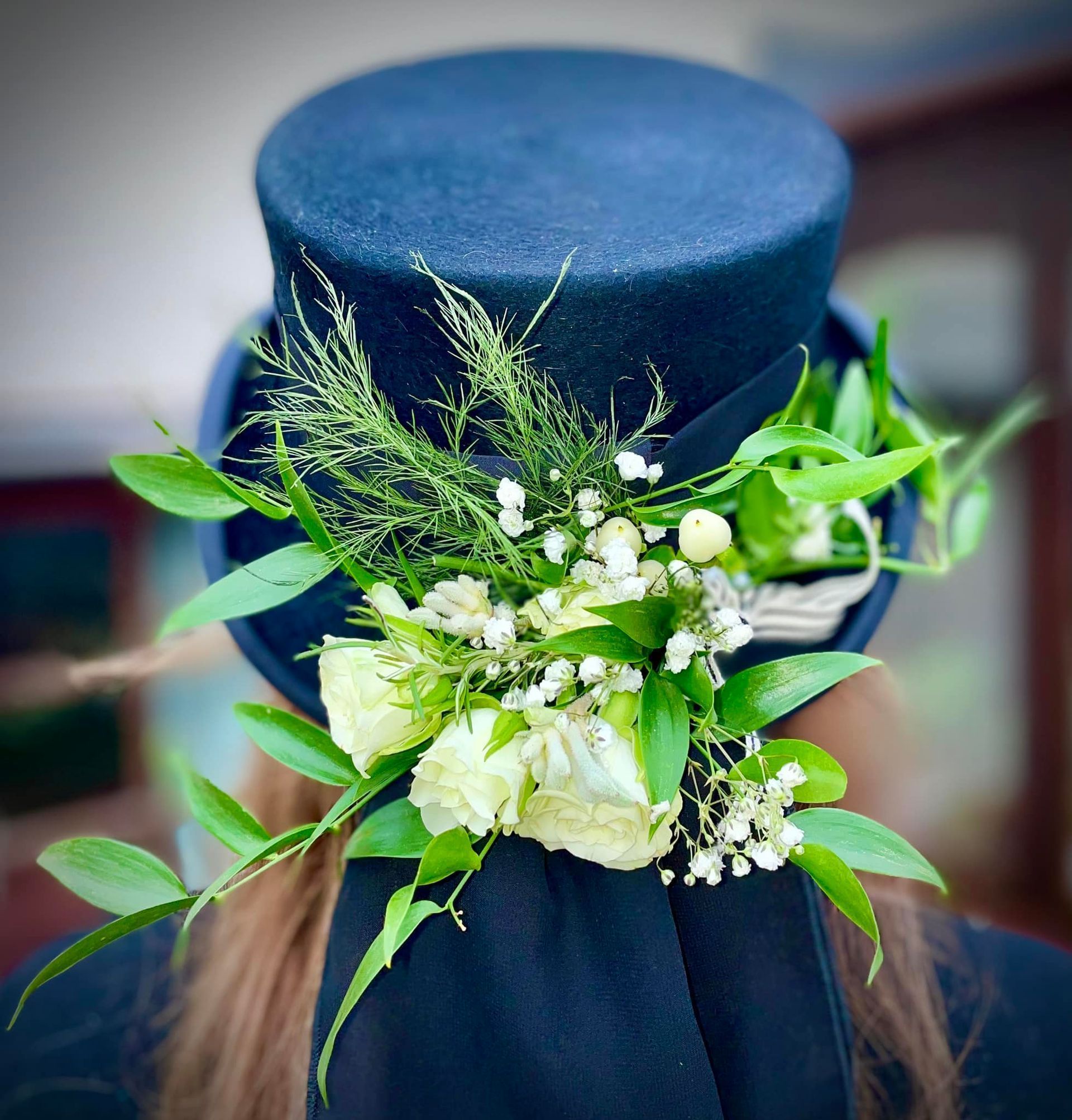 Woman wearing a dark blue top hat decorated with white flowers and greenery.