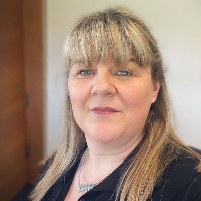 A woman with blonde hair is wearing a black shirt and a necklace.