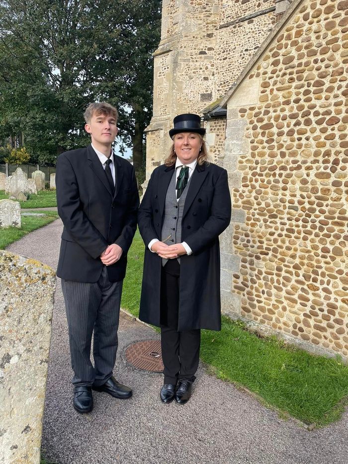 A man and a boy are standing next to each other in front of a stone wall.