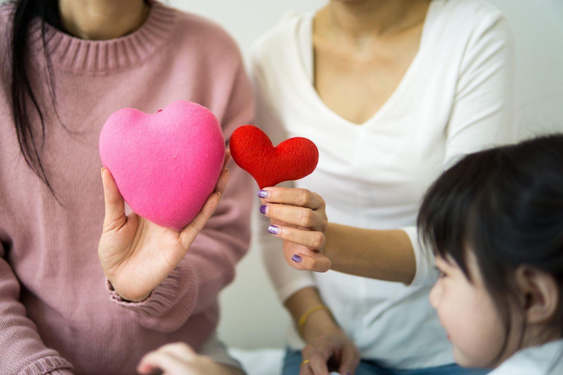 A woman is holding a pink heart next to a red heart