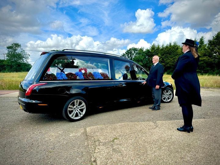 Two men are standing next to a black funeral car