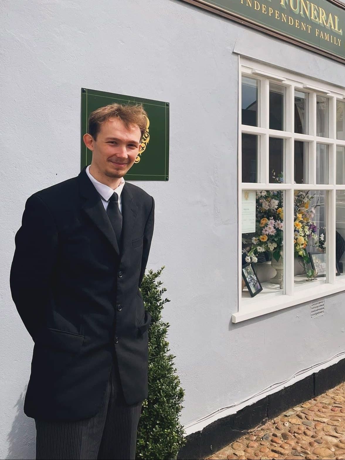 A man in a suit stands in front of a funeral home