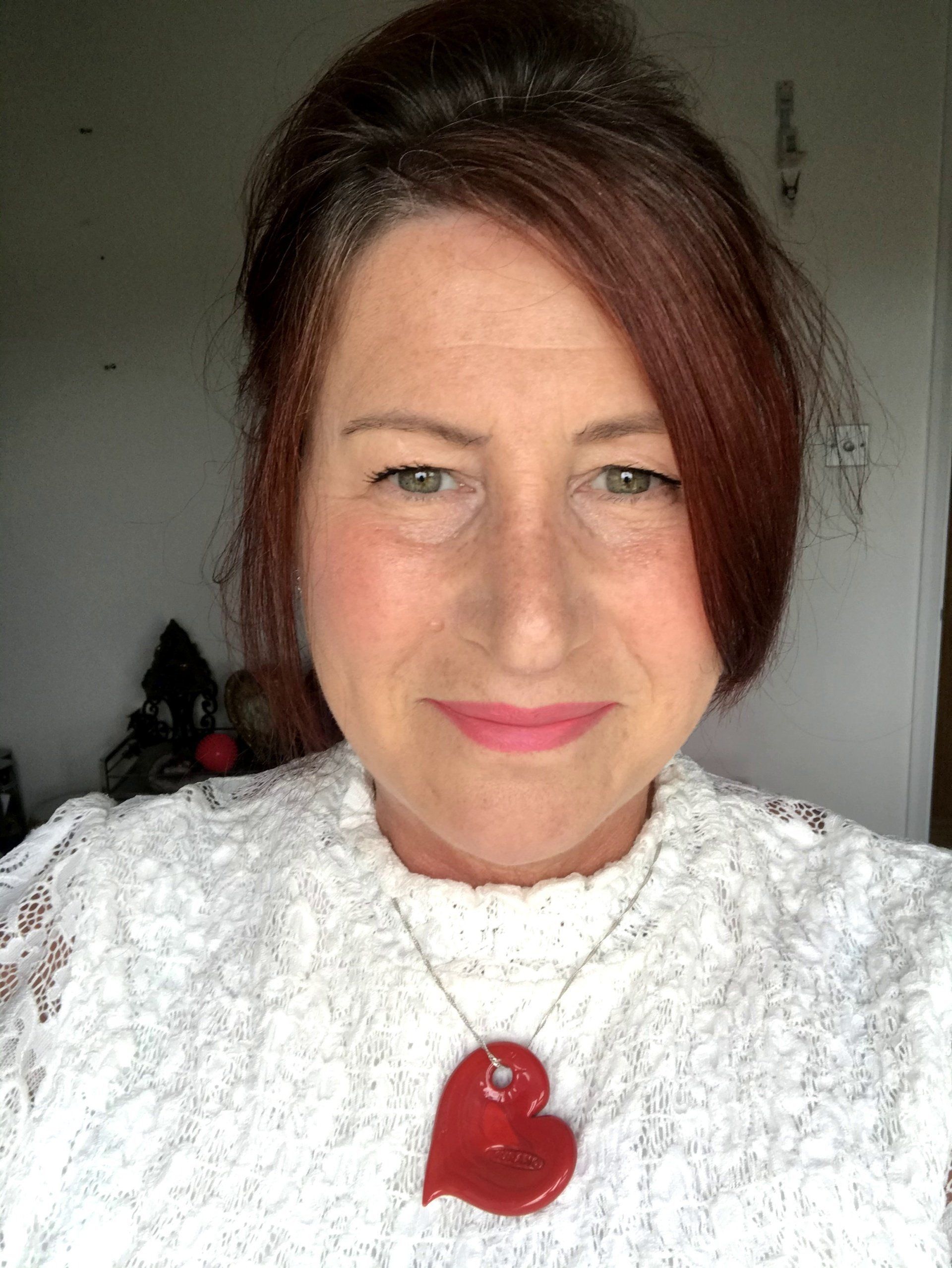 A woman is wearing a white sweater and a red heart necklace.