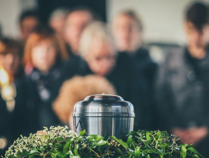 A group of people are standing around a urn at a funeral.