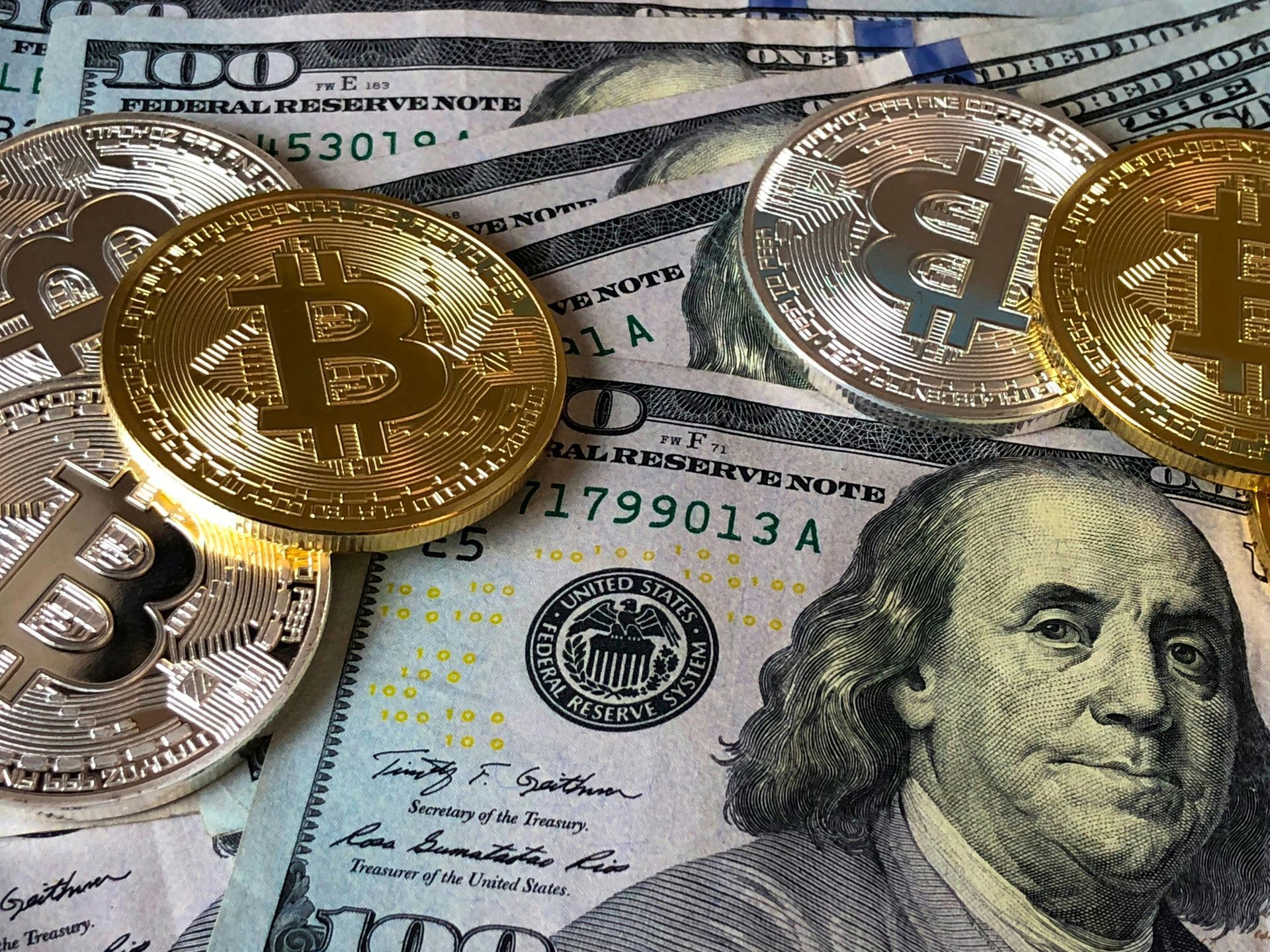 Bitcoin coins rest on top of US $100 bills.