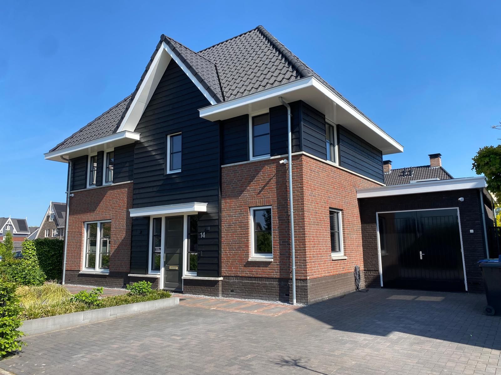 Een groot bakstenen huis met zwarte gevelbekleding en een garage
