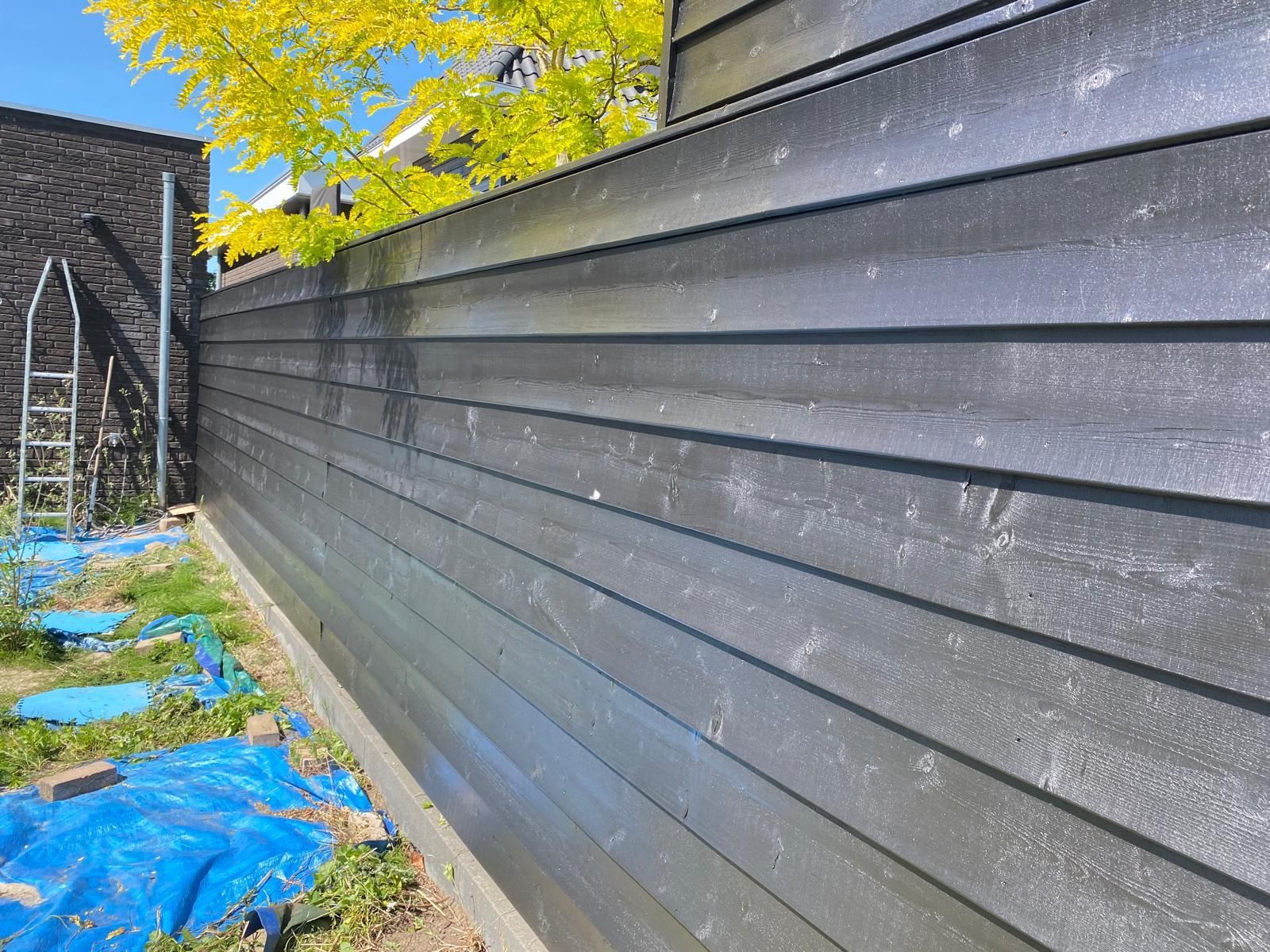 In een tuin wordt een zwart houten hek geschilderd.