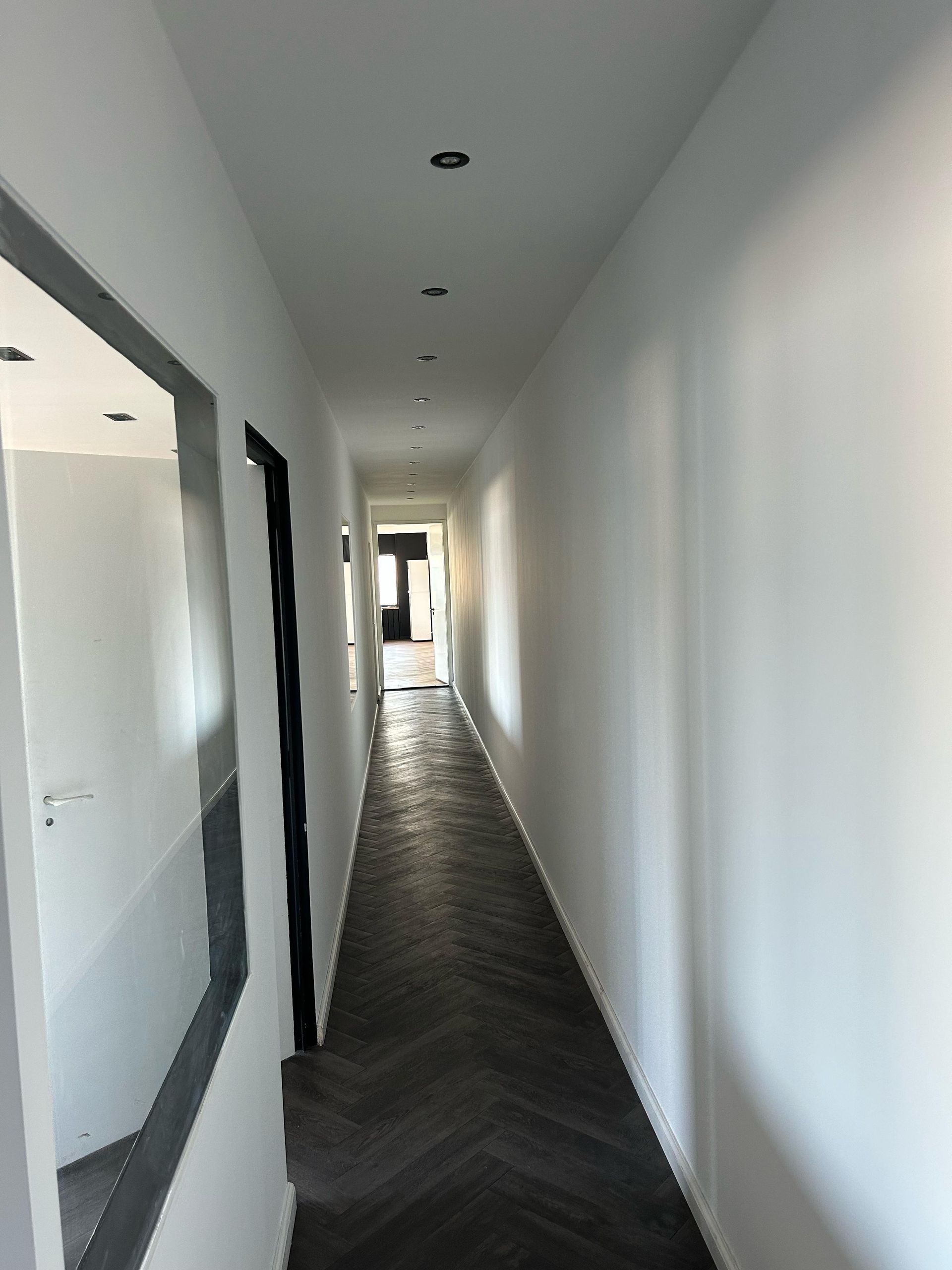 Een lange gang met een houten vloer en witte muren.